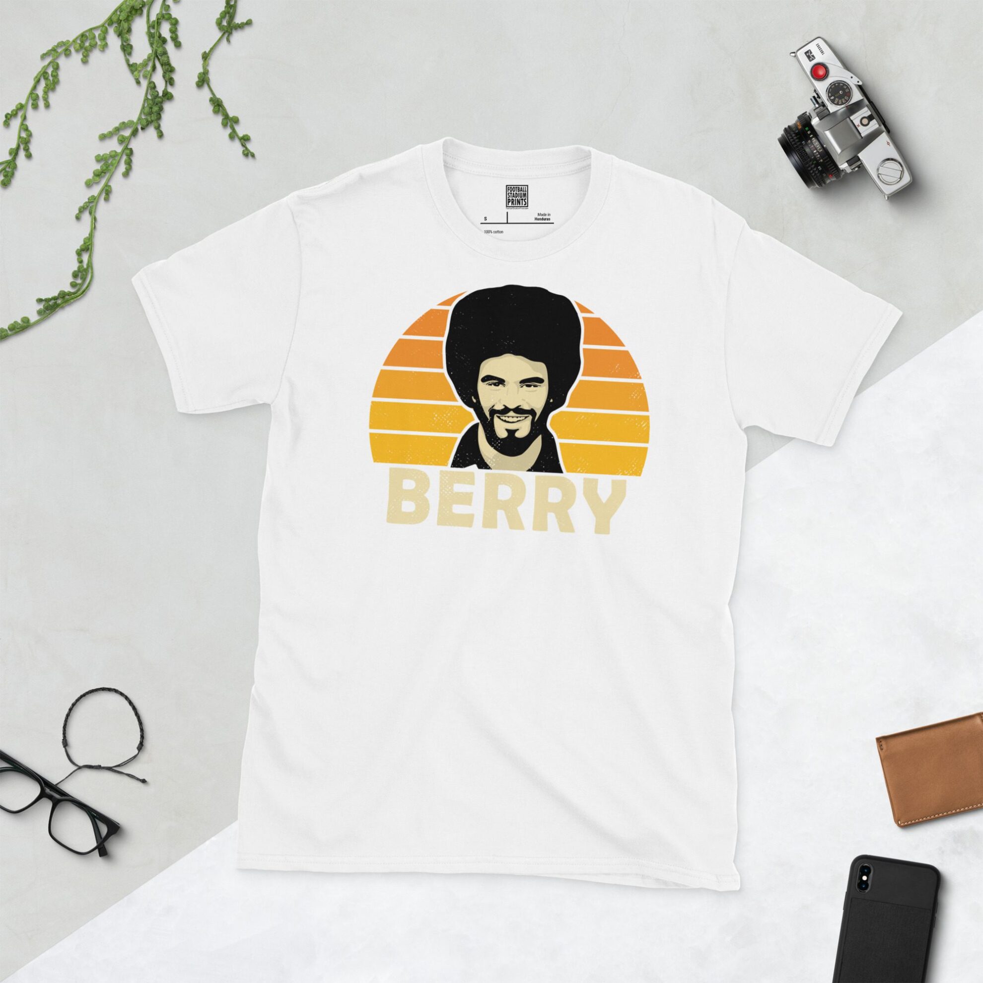 A white T-shirt with a bold portrait of football legend George Berry. The image is set against a Golden Orange sunburst background with the name "BERRY" in light yellow underneath.