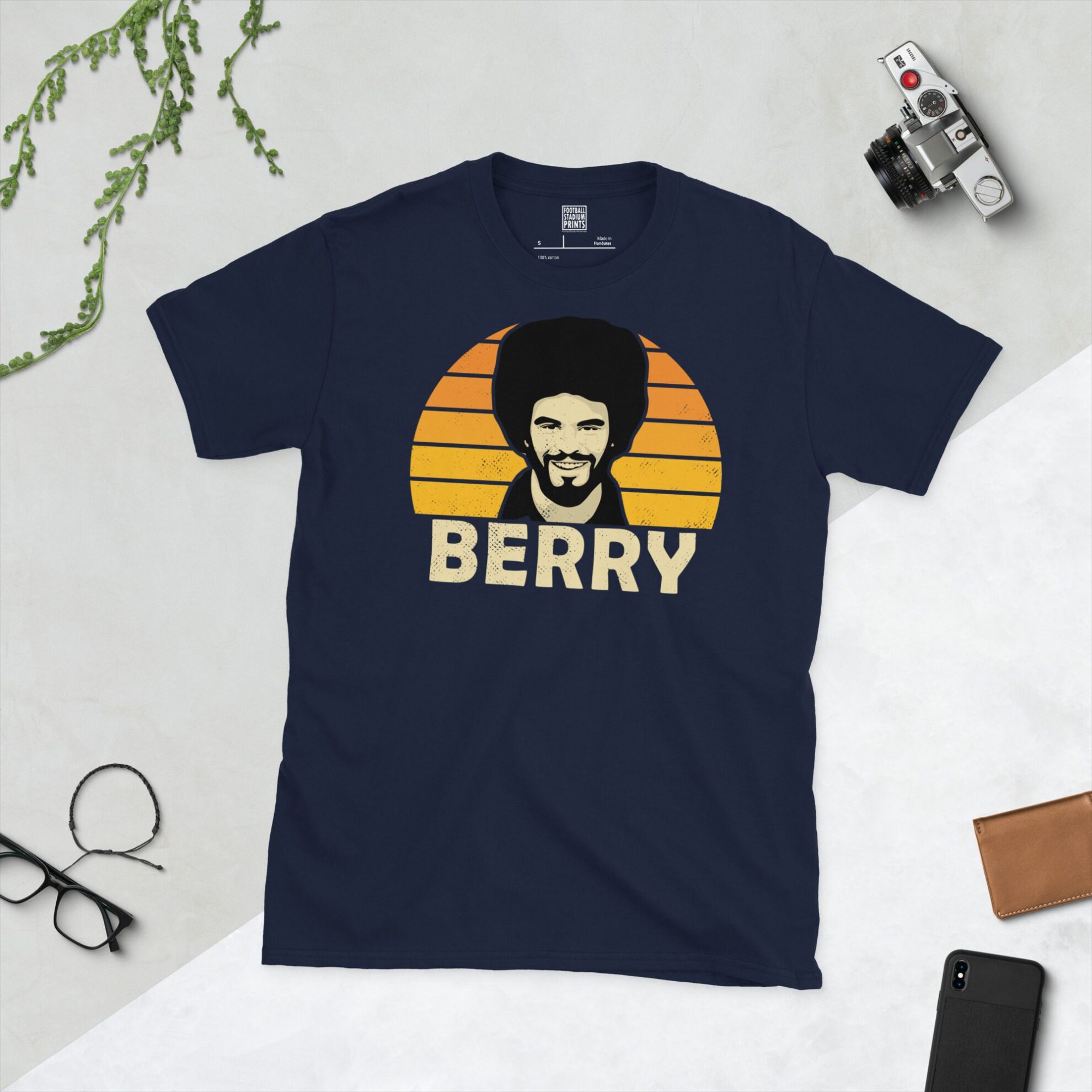 A navy T-shirt displaying an artistic illustration of George Berry, the former Wolves defender. The graphic is backed by a Golden Orange sunburst and the name "BERRY" appears underneath in light yellow.