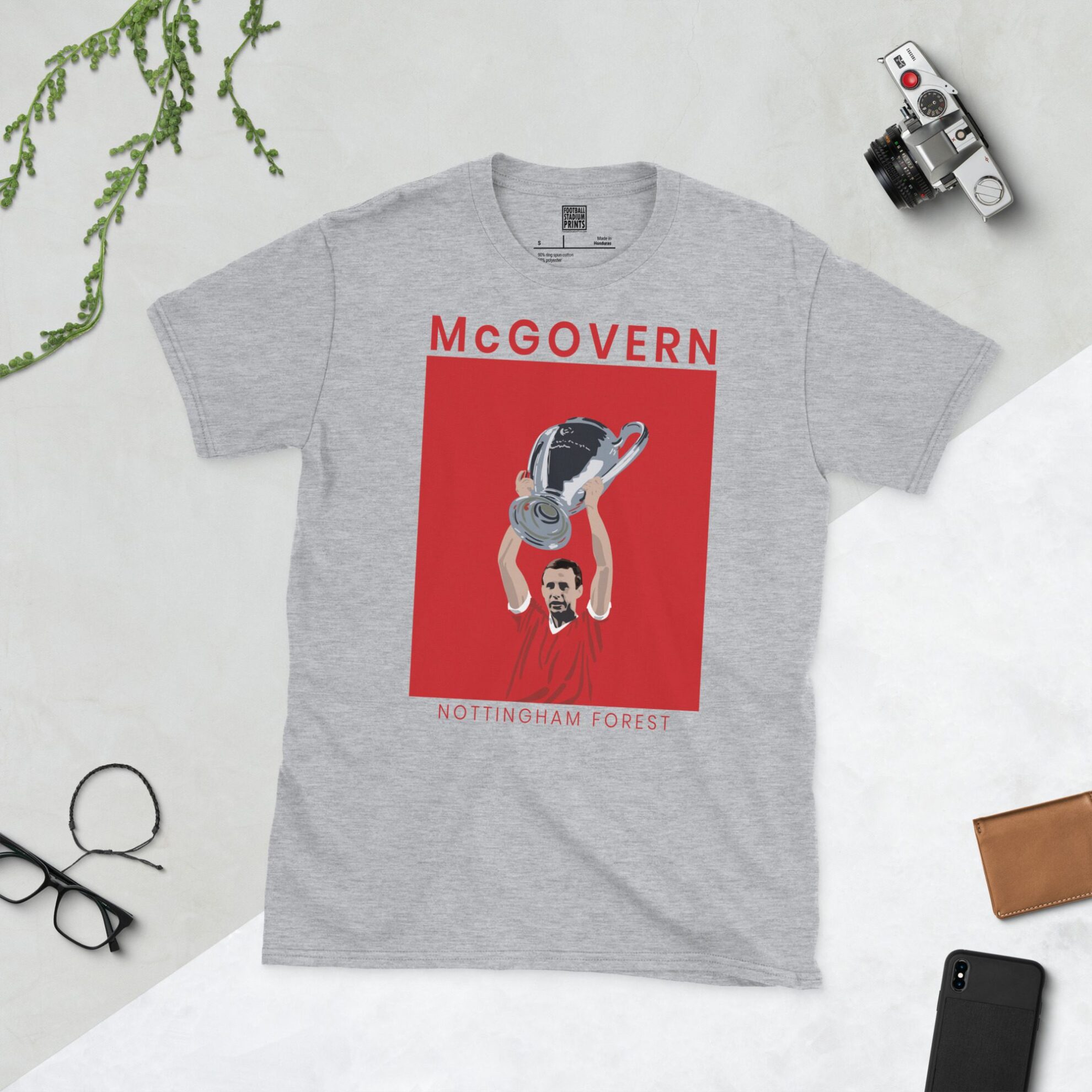 A sports grey T-shirt featuring a clean white graphic of Nottingham Forest's John McGovern holding the trophy. The image is backed by a red and white sunburst and the text "MCGOVERN" is printed below the portrait.