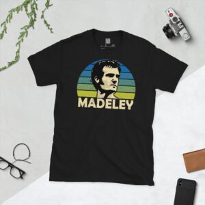 A black T-shirt featuring a stylised graphic of Leeds United legend Paul Madeley's profile, set against a blue to yellow faded striped sunburst background. The name "MADELEY" is printed in light yellow below the portrait.
