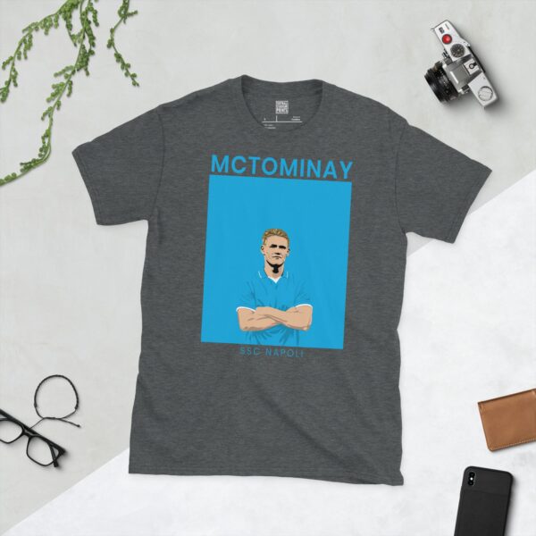 A dark heather T-shirt showing a clean, modern portrait of Scott McTominay, themed around SSC Napoli's light blue colour, with "MCTOMINAY" above and "SSC NAPOLI" below.