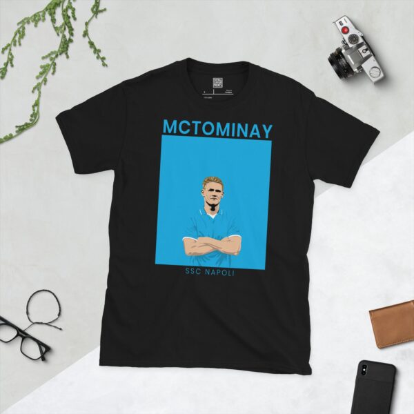 A black T-shirt featuring a modern, stylised graphic of footballer Scott McTominay in a light blue SSC Napoli-themed kit, with his arms crossed. "MCTOMINAY" is above the image and "SSC NAPOLI" is below.