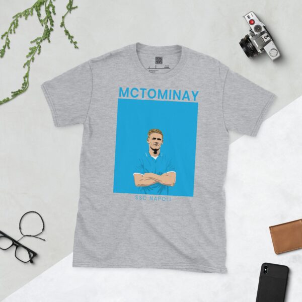 A sports grey T-shirt featuring a unique graphic of Scott McTominay in a light blue football shirt. The text "MCTOMINAY" is above his image and "SSC NAPOLI" is below.