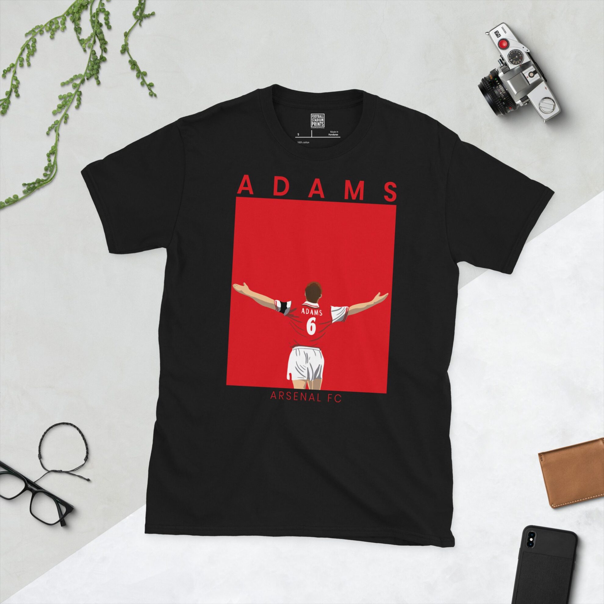 A black T-shirt featuring a graphic of Arsenal FC legend Tony Adams from behind, wearing the number 6 shirt with his arms raised. "ADAMS" is above the image and "ARSENAL FC" is below, on a bold red background.