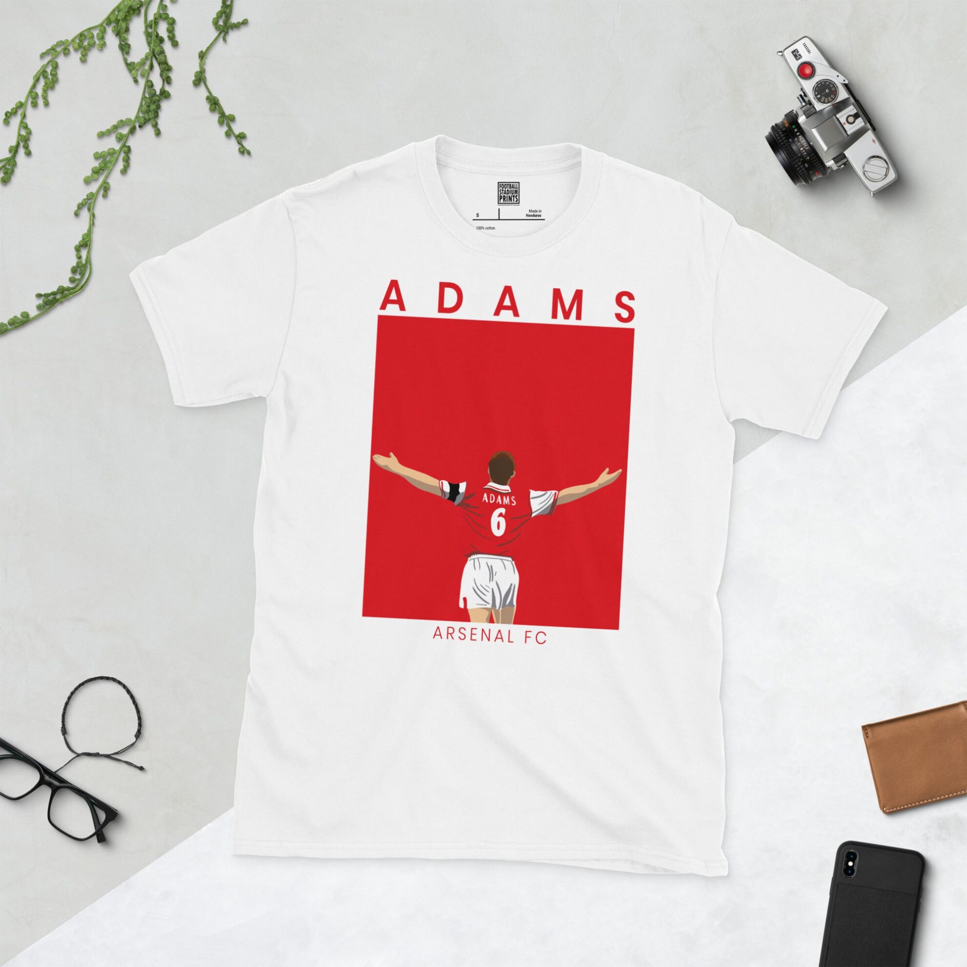A white T-shirt with a contemporary graphic of Tony Adams celebrating a goal for Arsenal. The text "ADAMS" is above and "ARSENAL FC" is below the image, set against a solid red backdrop.