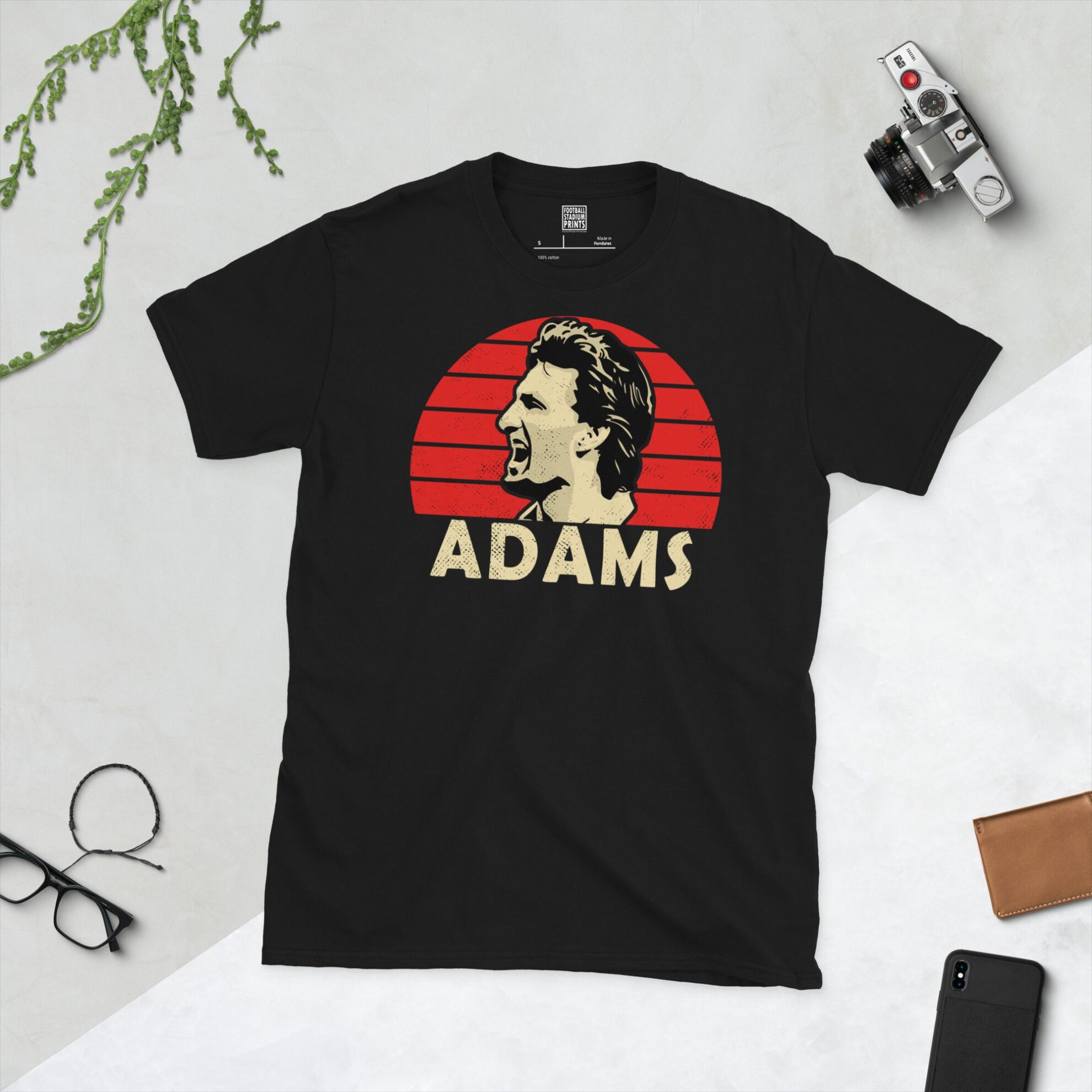A black T-shirt featuring a distressed, retro graphic of Arsenal legend Tony Adams' profile against a red striped sunburst. The name "ADAMS" is printed in yellow lettering below the portrait.