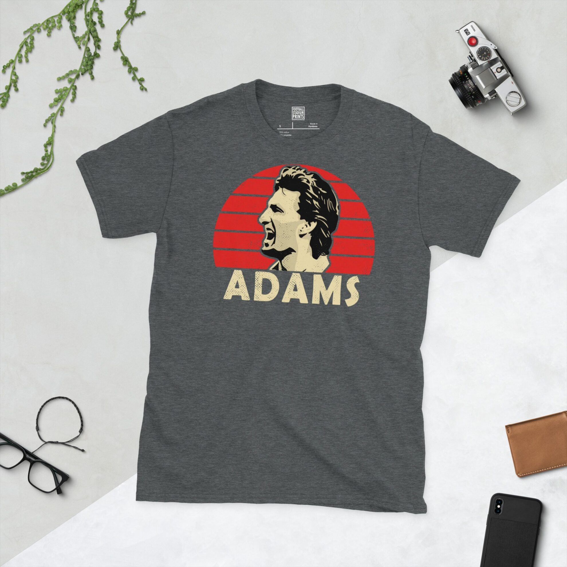 A dark heather T-shirt showing a clean, distressed portrait of Tony Adams, the Arsenal legend, with "ADAMS" printed in yellow below the image on a red sunburst background.