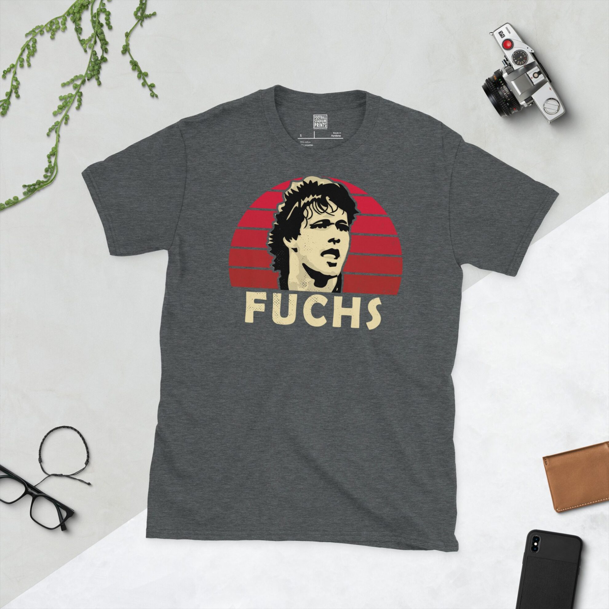 A dark heather T-shirt showing a clean, modern portrait of Uwe Fuchs, the Boro icon, with "FUCHS" printed in light yellow below the image on a red sunburst background.
