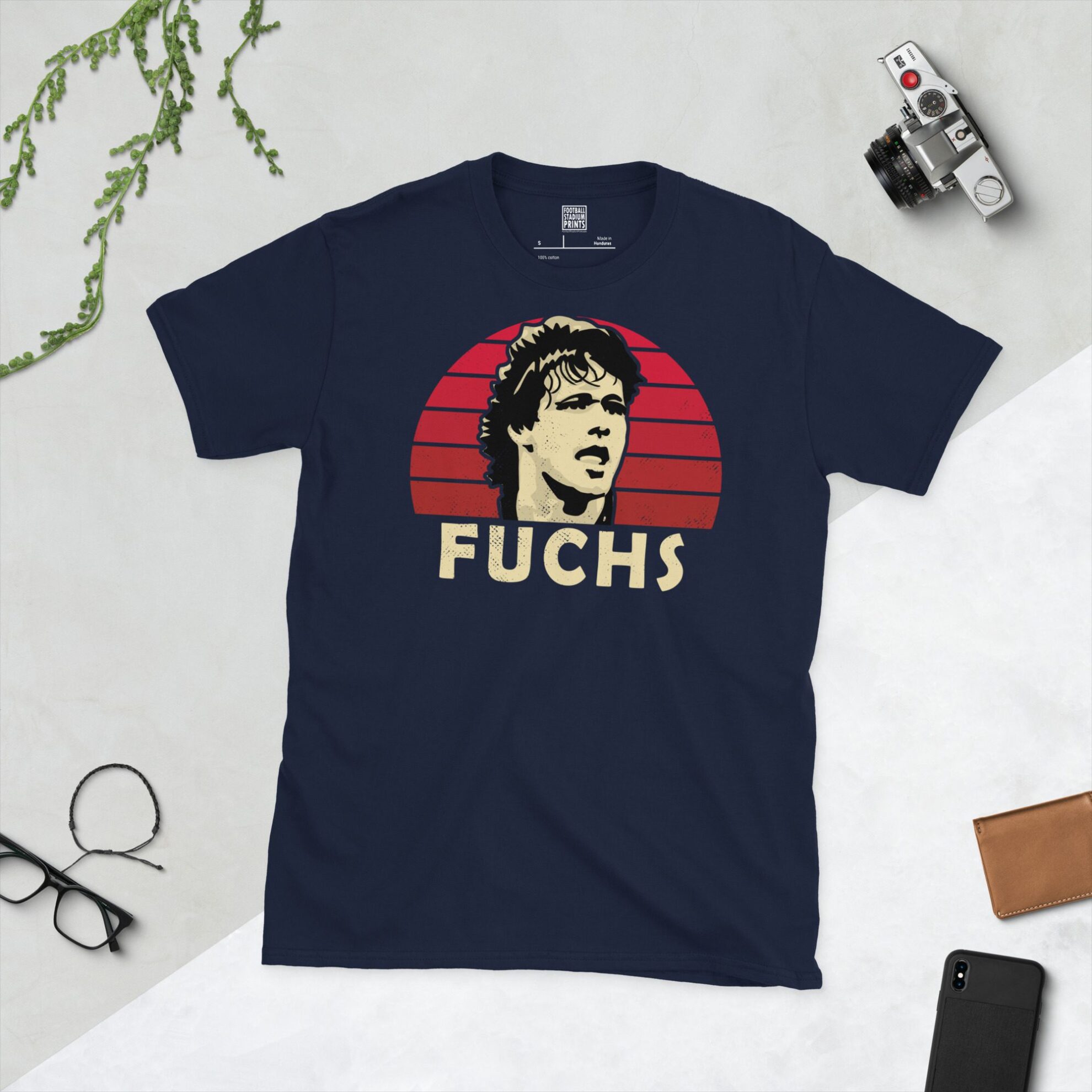 A navy T-shirt displaying an artistic illustration of Uwe Fuchs, the former Middlesbrough striker. The graphic is backed by a red sunburst and the name "FUCHS" appears underneath in light yellow.