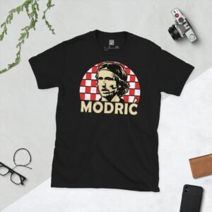 A black T-shirt featuring a stylised, distressed graphic of Croatia legend Luka Modrić's portrait, set against a red and white checkered sunburst background. The name "MODRIĆ" is printed in white below the portrait.