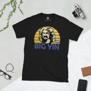 A black T-shirt featuring a stylised, distressed graphic of comedian Billy Connolly. The portrait is backed by a yellow sunburst referencing his banana boots, with the text "BIG YIN" printed in purple below.