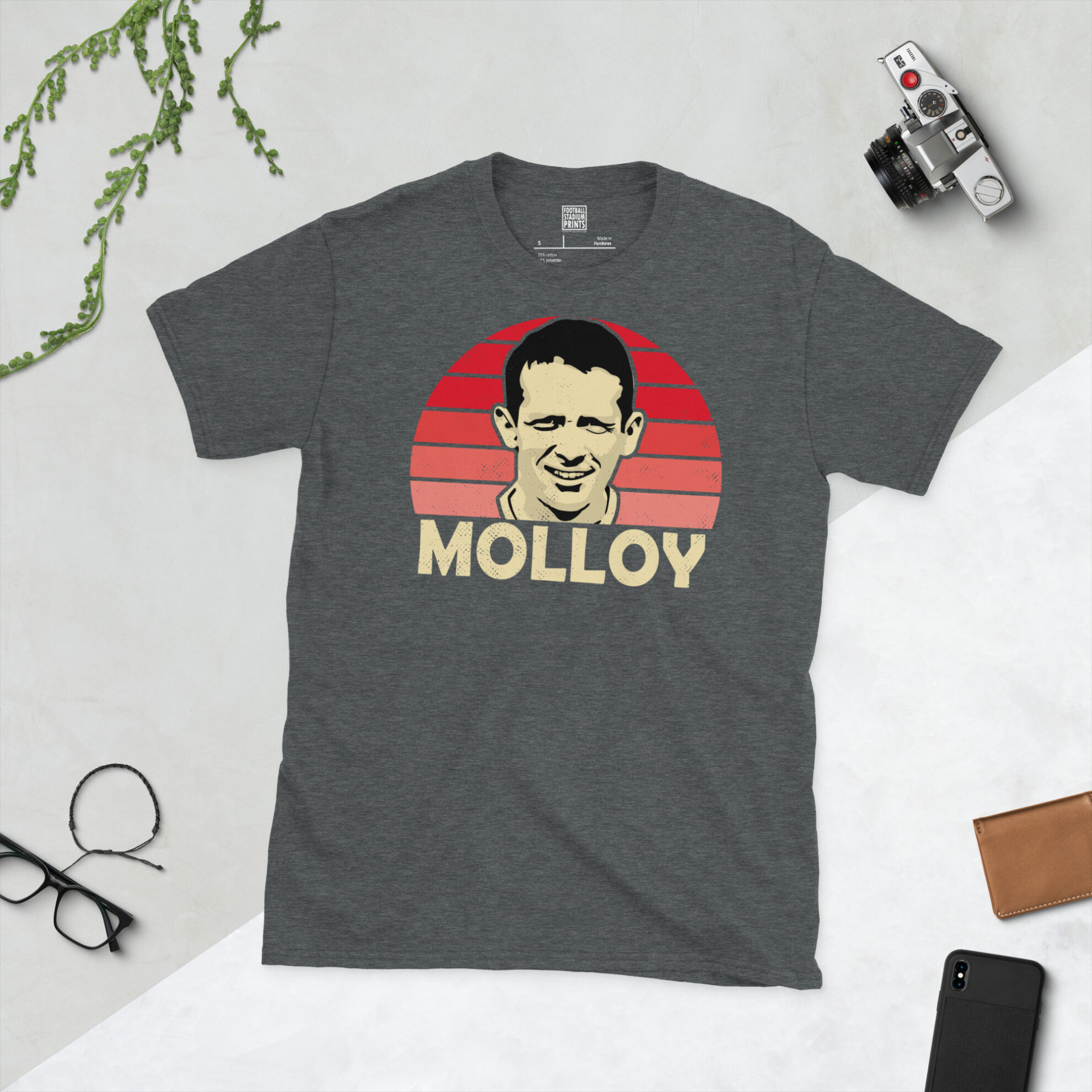 A dark heather T-shirt showing a clean, modern portrait of Craig Molloy, the Brechin City icon, with "MOLLOY" printed in light yellow below the image on a red sunburst background.