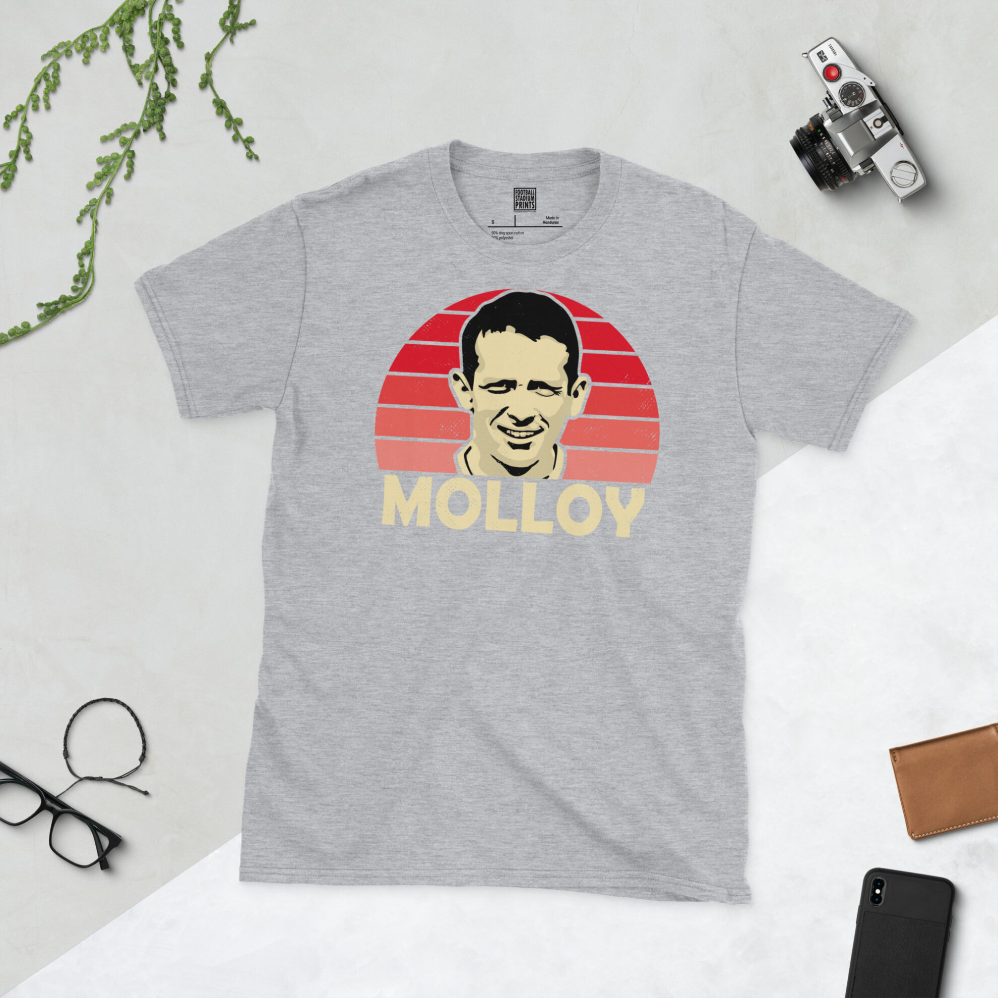 A sports grey T-shirt featuring a unique graphic of Craig Molloy. The image is backed by a red sunburst and the text "MOLLOY" is printed below the portrait in light yellow.
