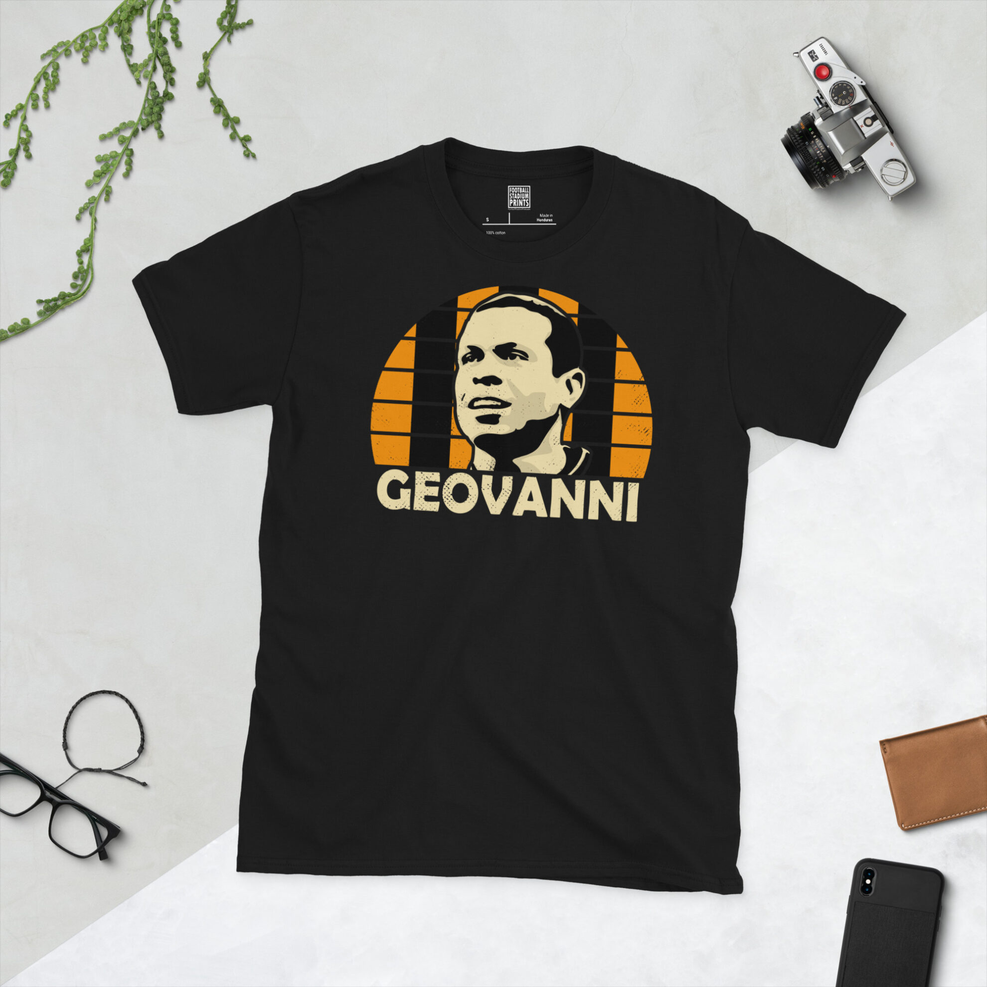 A black T-shirt featuring a stylised, distressed graphic of Hull City legend Geovanni. The portrait is backed by an amber and black striped sunburst, with the name "GEOVANNI" printed in light yellow below.