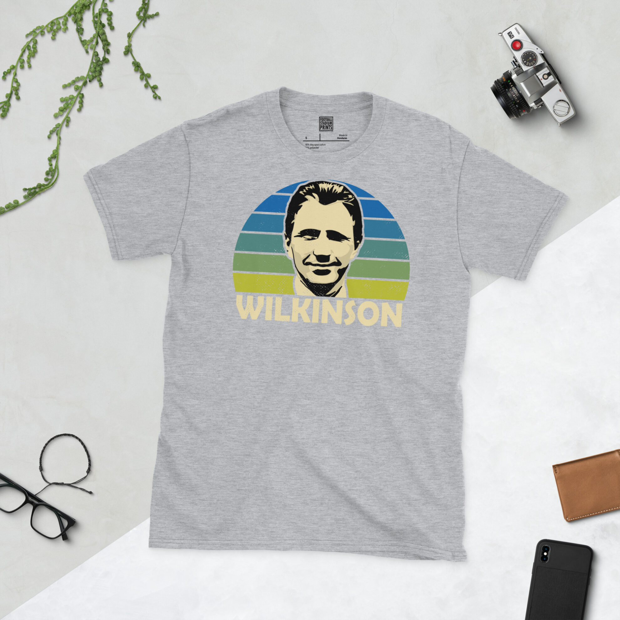 A sports grey T-shirt featuring a unique graphic of Howard Wilkinson. The image is backed by a blue to yellow sunburst and the text "WILKINSON" is printed below the portrait in white.