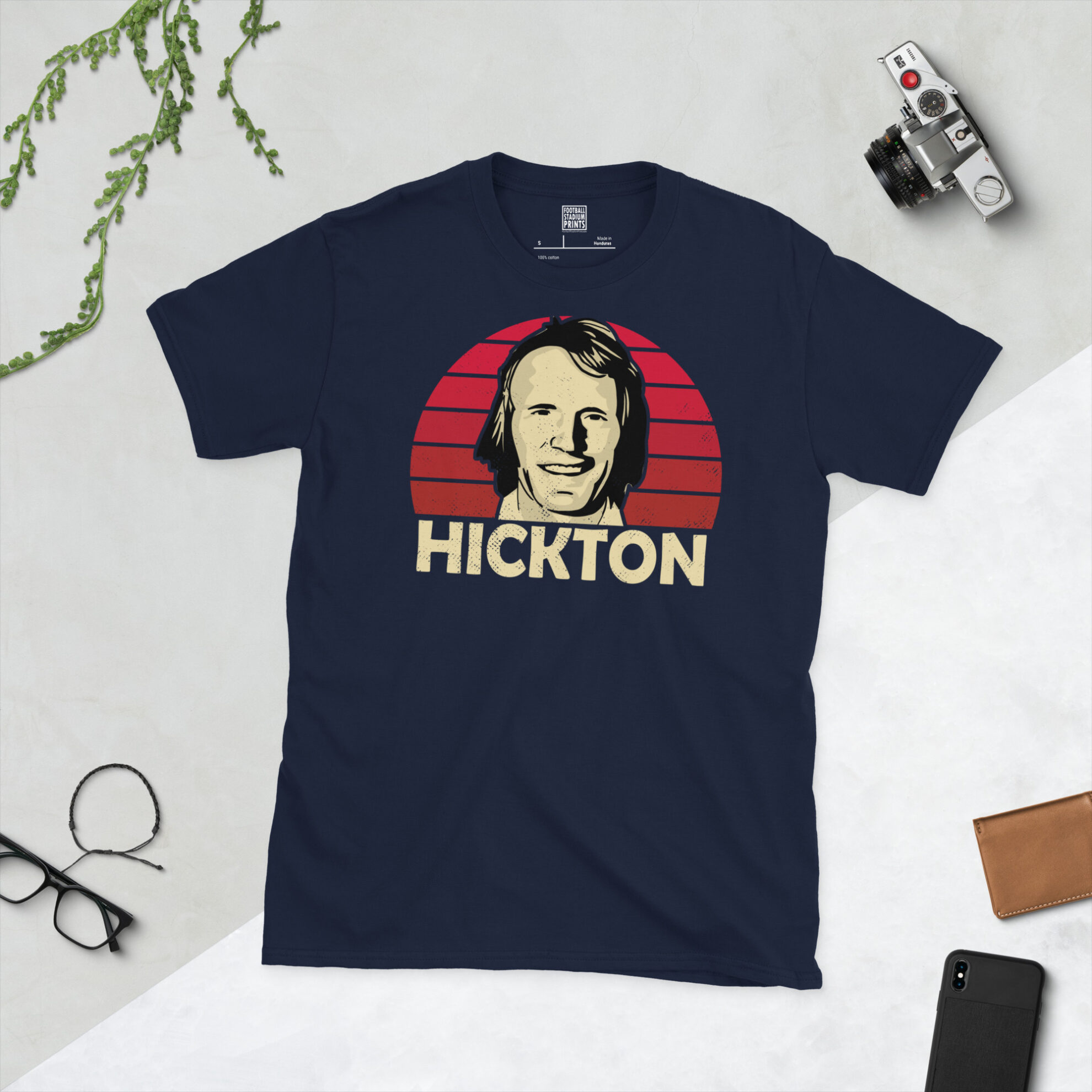 A navy T-shirt displaying an artistic illustration of John Hickton, the iconic Boro striker. The graphic features a red sunburst and the surname "HICKTON" appears underneath in light yellow.