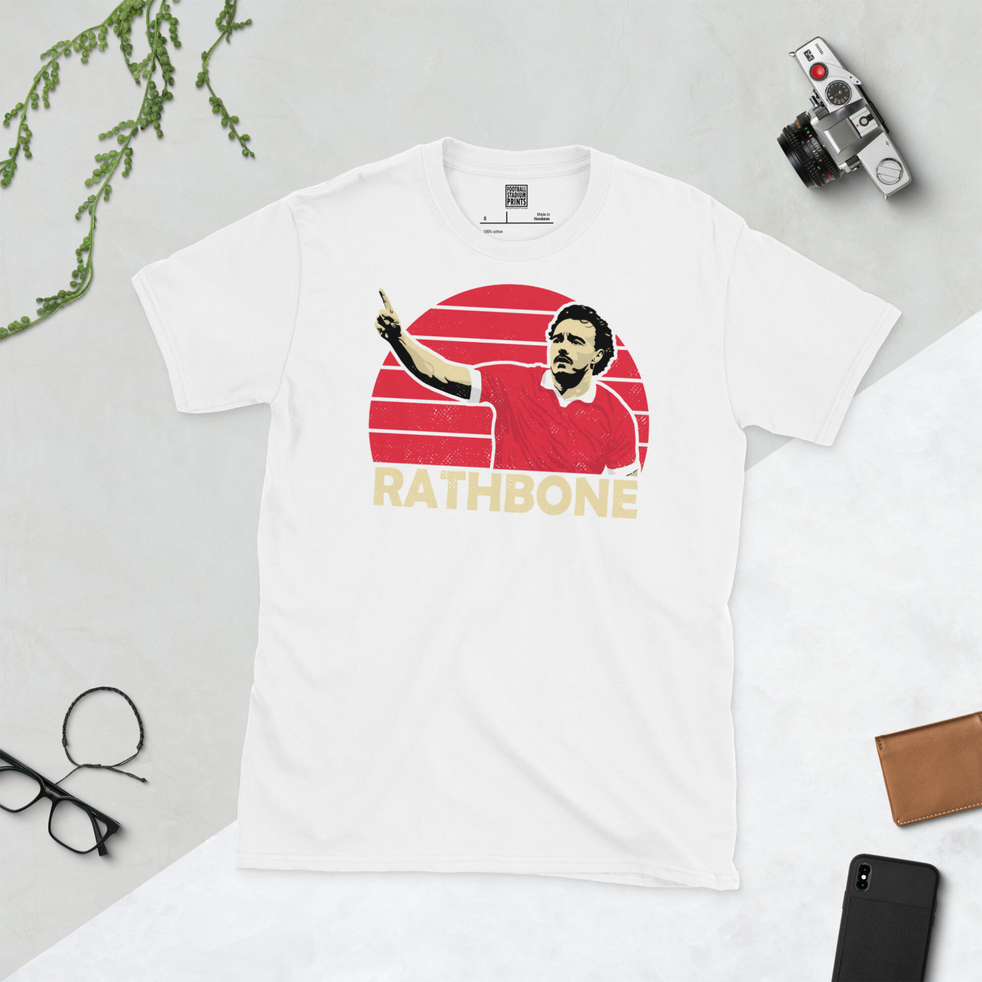 A white T-shirt with a bold, retro graphic of Wrexham star Ollie Rathbone. The image is set against a red sunburst background and the name "RATHBONE" is in light yellow underneath.