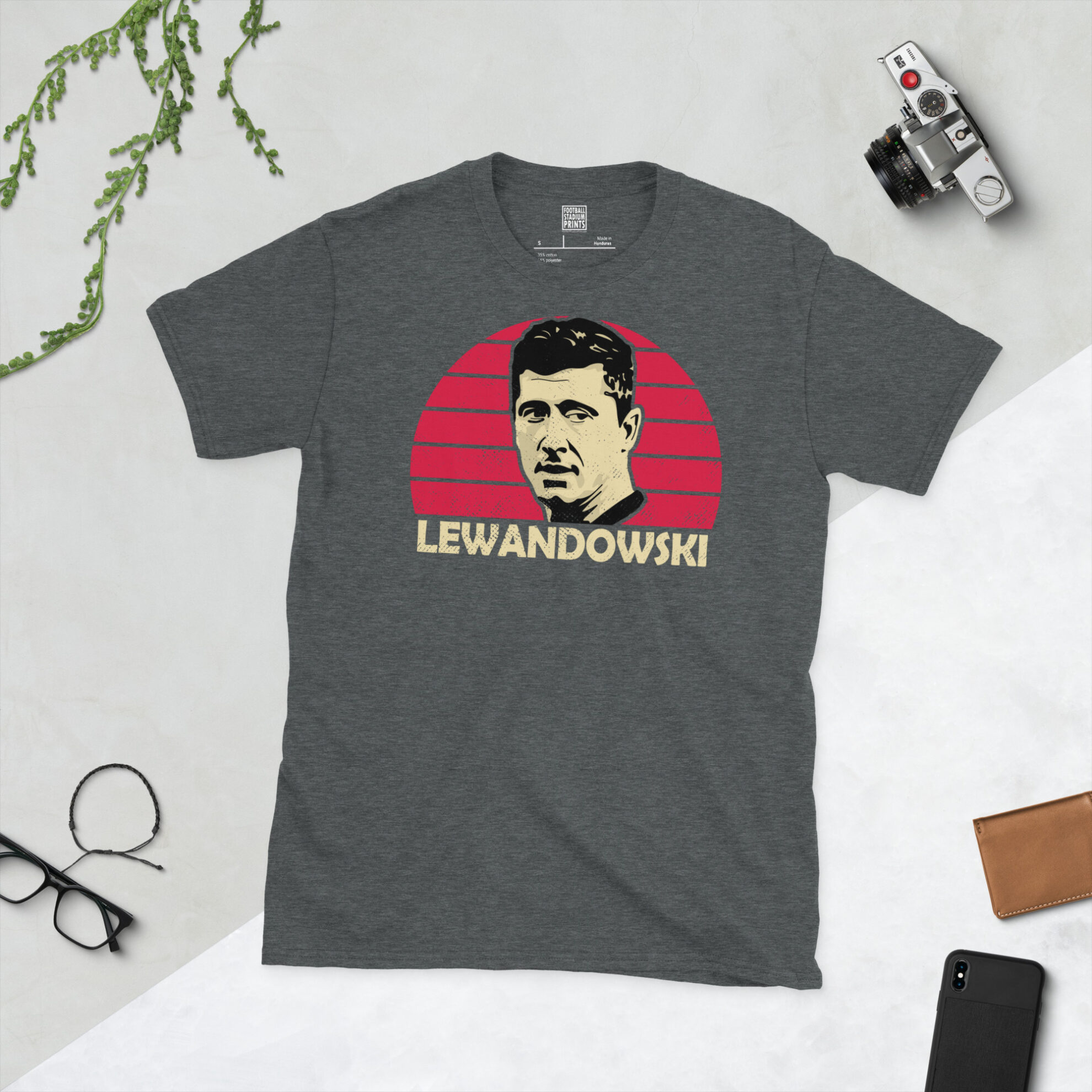 A dark heather T-shirt showing a clean, modern portrait of Robert Lewandowski, the Poland icon, with "LEWANDOWSKI" printed in light yellow below the image on a red sunburst background.