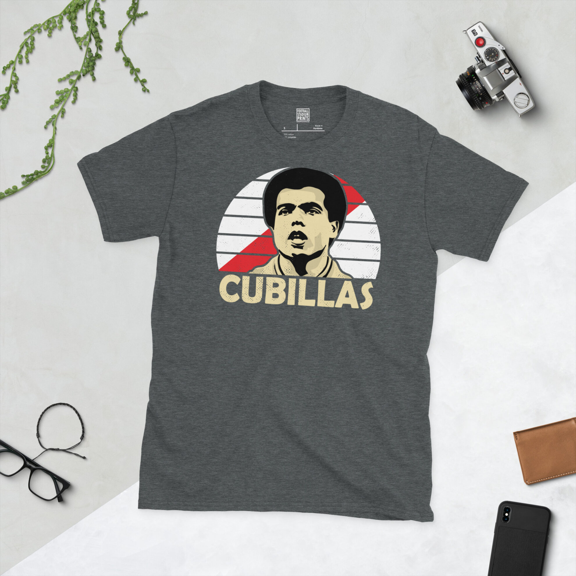 A dark heather T-shirt showing a clean, modern portrait of Teófilo Cubillas, the Peru icon, with "CUBILLAS" printed in light yellow below the image on a red sash sunburst background.