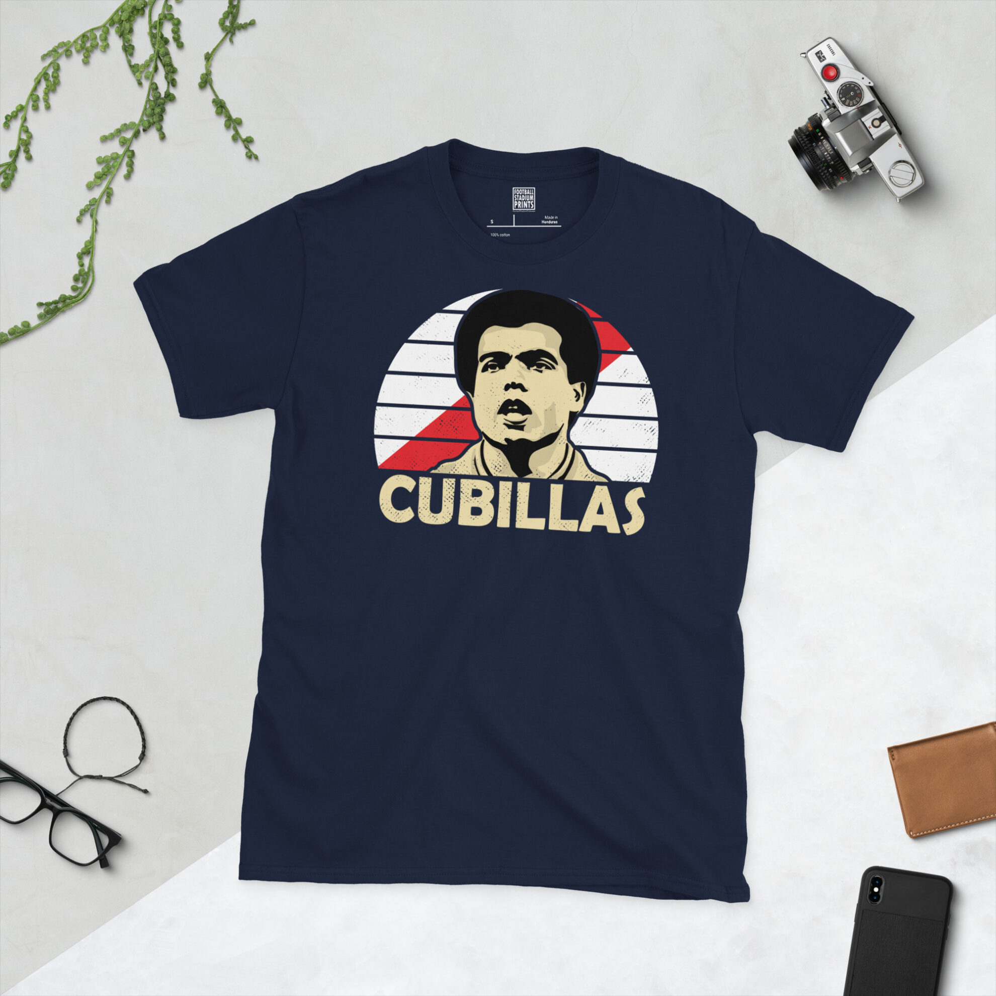 A navy T-shirt displaying an artistic illustration of Teófilo Cubillas, the former Peru playmaker. The graphic features a red sash sunburst and the surname "CUBILLAS" appears underneath in light yellow.