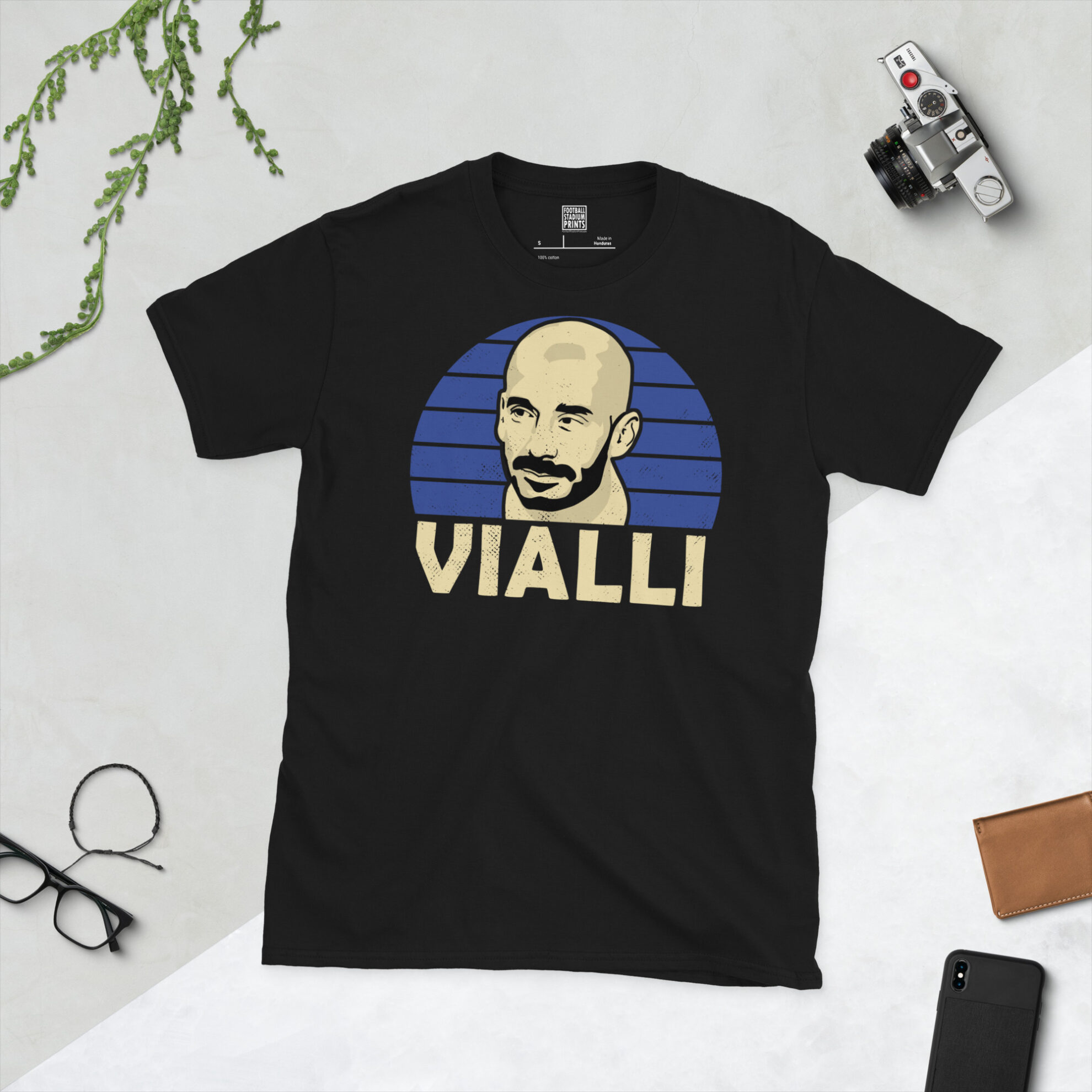 A black T-shirt featuring a stylised, distressed graphic of Chelsea legend Gianluca Vialli. The portrait is backed by a blue striped sunburst, with the name "VIALLI" printed in light yellow below.