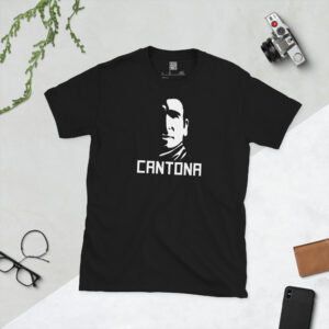 Flat lay of a black football t-shirt featuring a white, high-contrast half-face portrait of Eric Cantona with bold "CANTONA" text below.