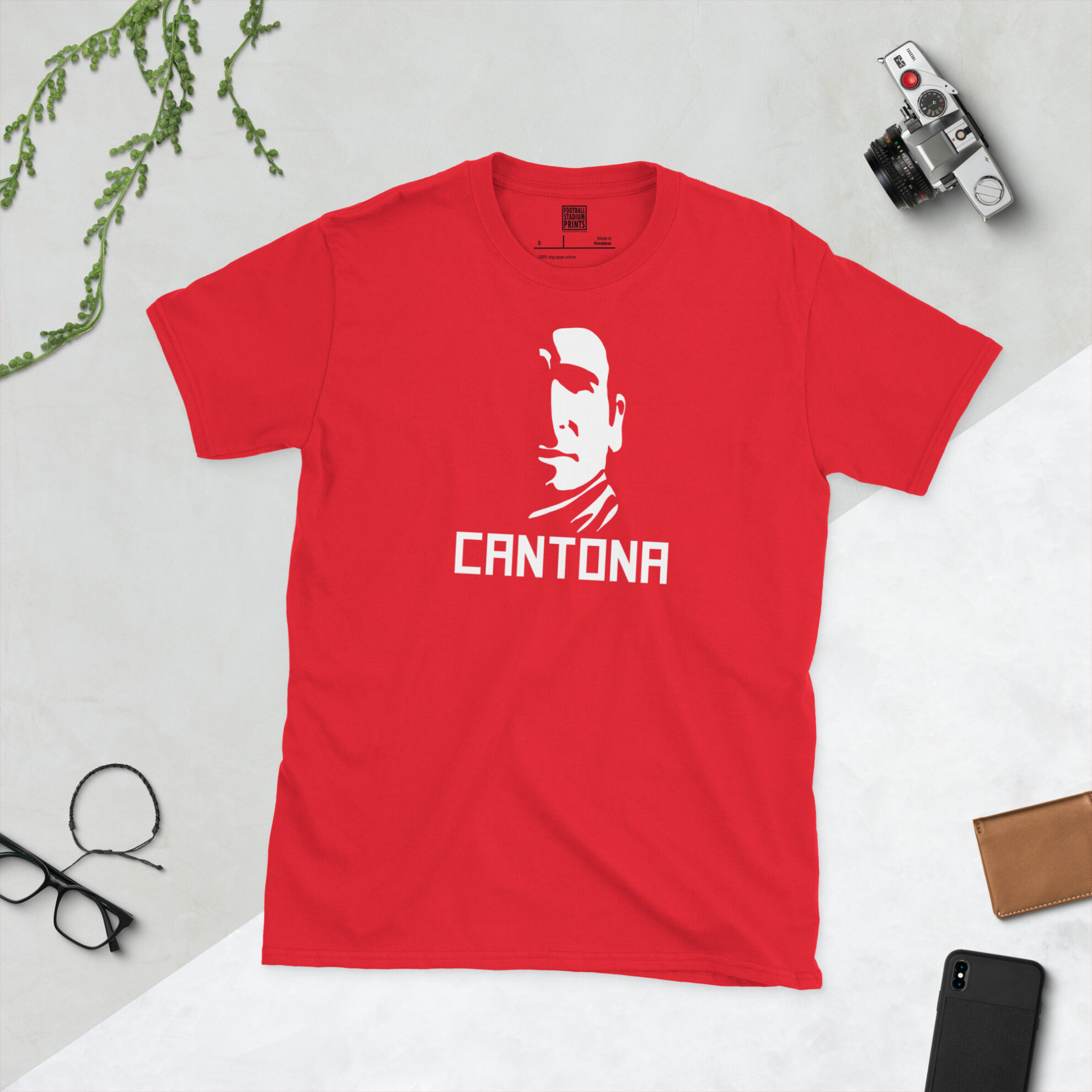 Flat lay of a red t-shirt with a striking white Eric Cantona portrait and "CANTONA" lettering, perfect for Manchester United fans.