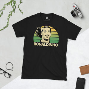 A black T-shirt featuring a stylised, distressed graphic of Brazilian legend Ronaldinho. The portrait is backed by a yellow to green fade sunburst, with the name "RONALDINHO" printed in light yellow below.