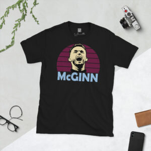 A premium black T-shirt featuring a distressed claret sunburst graphic of Aston Villa captain John McGinn with his name in bold sky blue text.