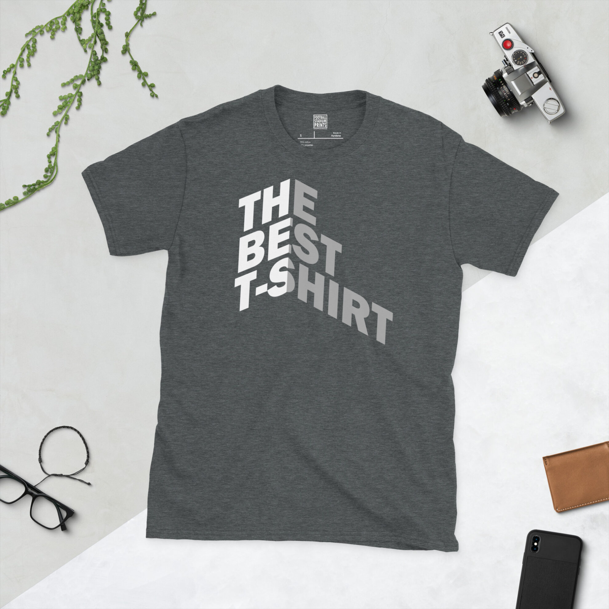 A dark heather t-shirt with Bold white and gray text reading THE BEST T-SHIRT folded around a 3D isometric corner against a black background