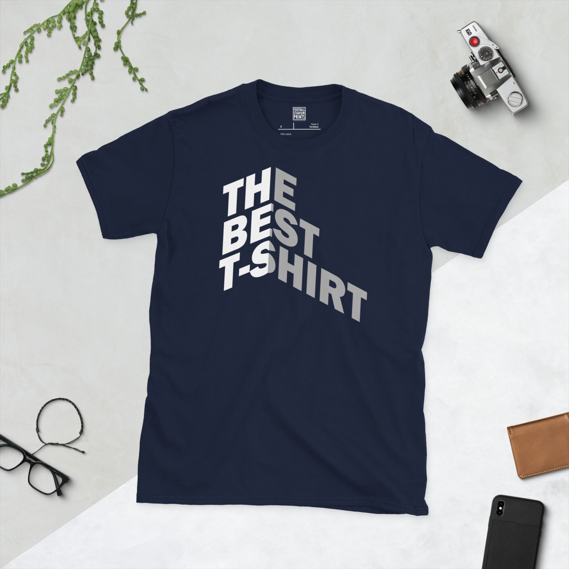A navy t-shirt with Bold white and gray text reading THE BEST T-SHIRT folded around a 3D isometric corner against a black background