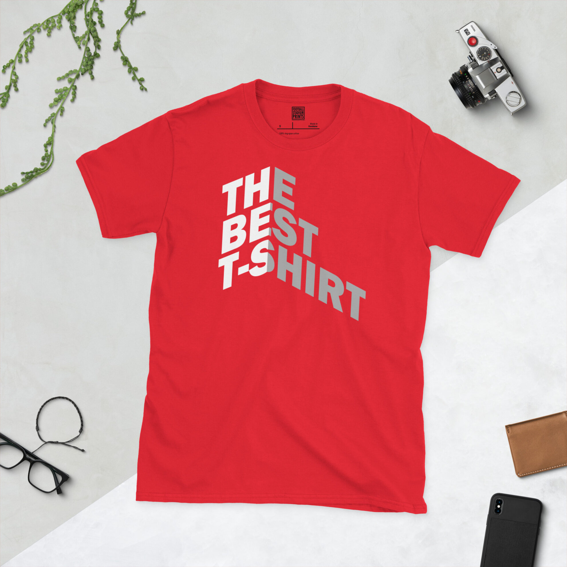 A red t-shirt with Bold white and gray text reading THE BEST T-SHIRT folded around a 3D isometric corner against a black background