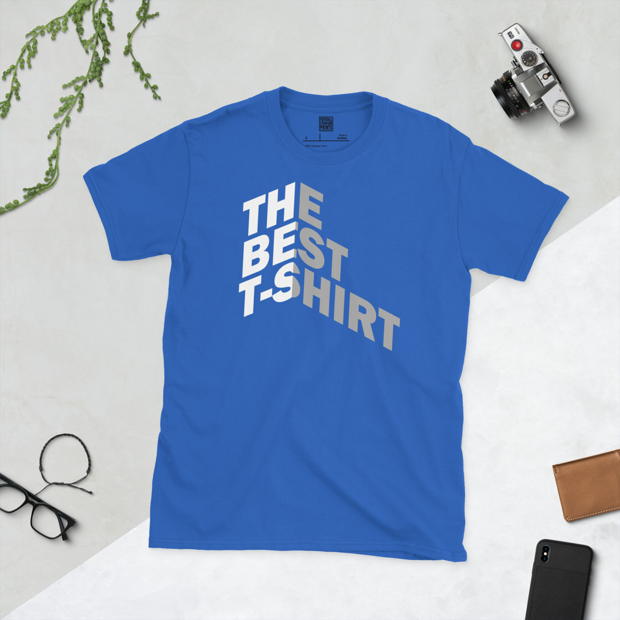 A blue t-shirt with Bold white and gray text reading THE BEST T-SHIRT folded around a 3D isometric corner against a black background