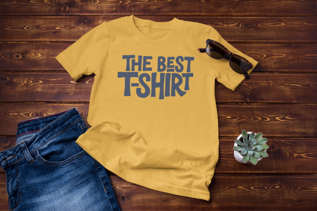 Gold yellow graphic t-shirt laid flat with dark grey rounded text reading The Best T-Shirt