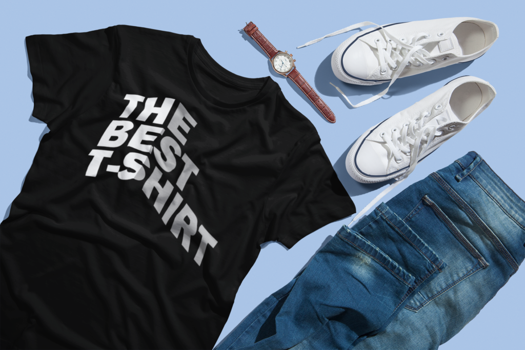 Black graphic tee laid out with white 3D perspective typography reading The Best T-Shirt alongside jeans and white sneakers